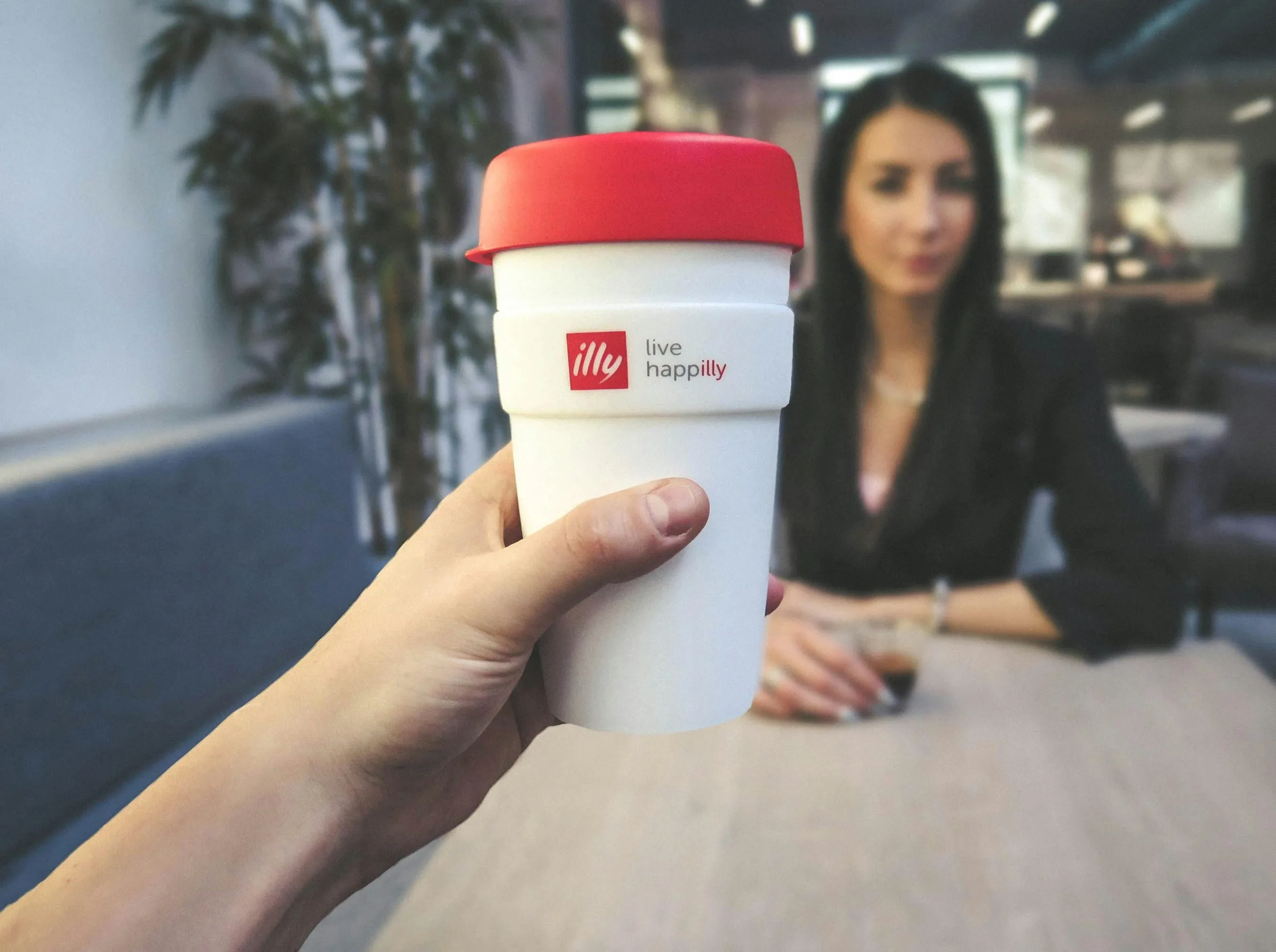 A hand holding a branded coffee cup with the logo "illy live happilly" in focus, highlighting the importance of a strong small business brand strategy in Singapore to create memorable customer connections.